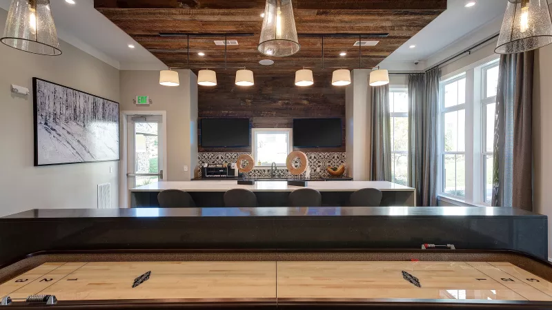 Clubroom with shuffleboard table, bar seating, and wood-accent ceiling at Avery Turkey Creek Apartments.