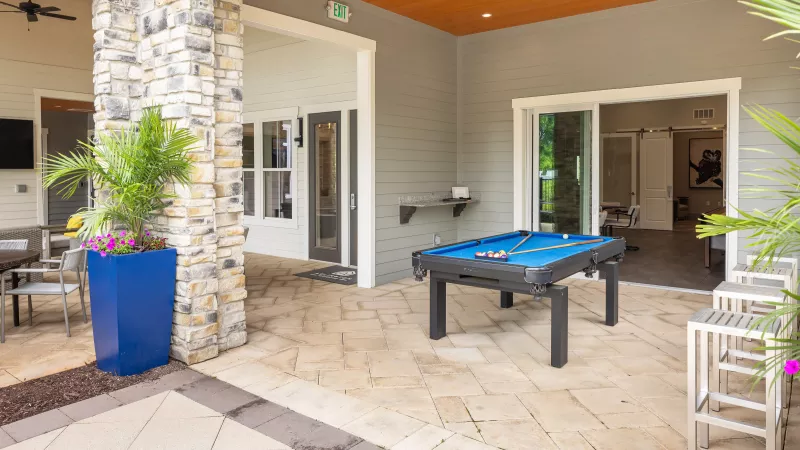 Covered outdoor lounge at Avery apartments with pool table, stone columns, and modern seating area.