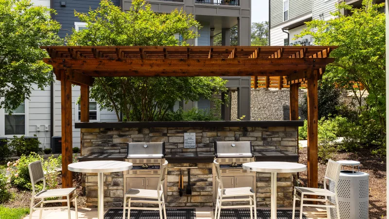 Outdoor grilling station at Avery at Turkey Creek Apartments with pergola, stone backsplash, and stainless steel grills.