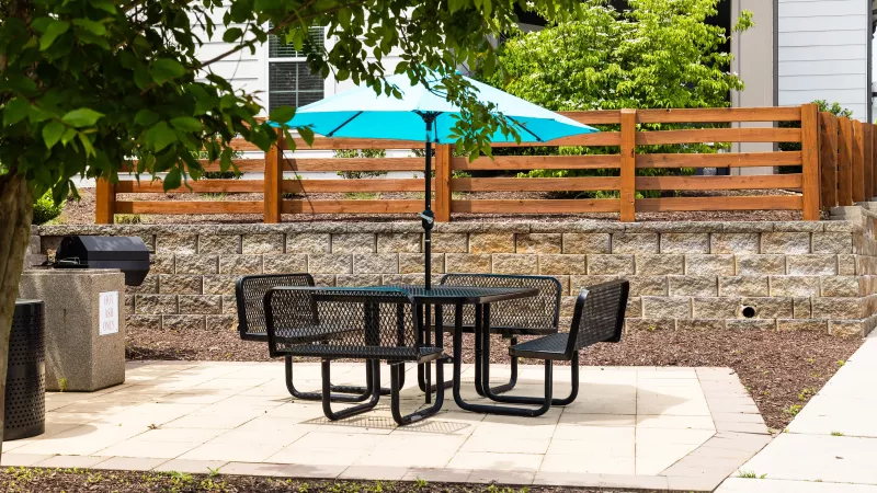 Shaded picnic table with umbrella and grill at Avery at Turkey Creek Apartments.
