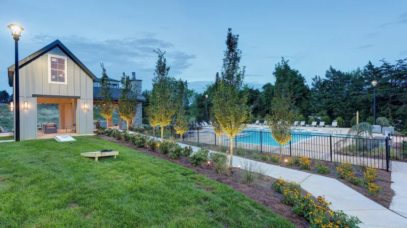 Evening view of pool and pavilion with cornhole lawn game and landscaped gardens at Avery at Turkey Creek Apartments.