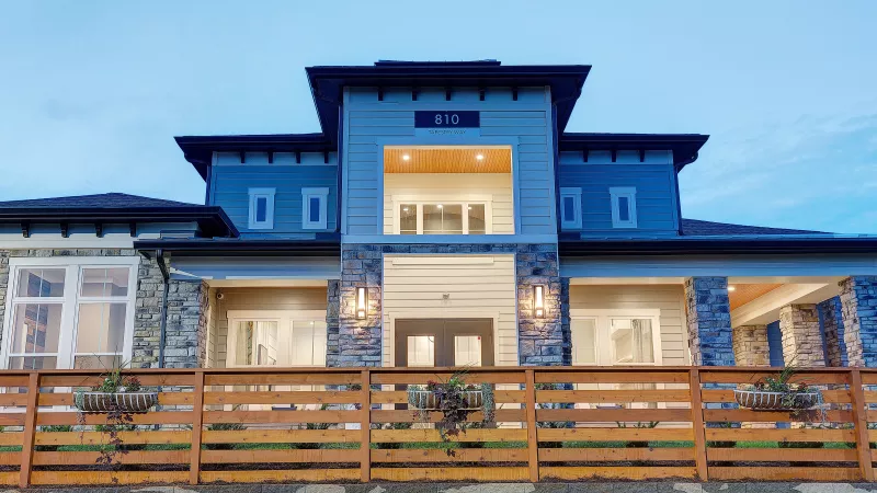 Clubhouse exterior at Avery at Turkey Creek Apartments with stone accents, wood fence, and modern lighting at dusk.