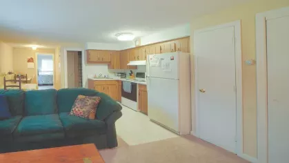 Royal Crest Estates Marlboro open kitchen and living area – Open-layout kitchen and living space with wood cabinets, full-size refrigerator, and cozy seating.