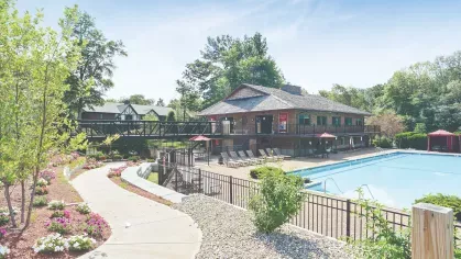 Community pool with landscaped walkway – Outdoor swimming pool next to clubhouse, landscaped flowers, and paved walking paths at Royal Crest Estates Marlboro.