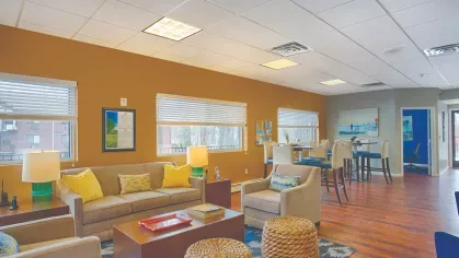 Royal Crest Estates Marlboro lounge with comfortable seating, yellow accent pillows, wood floors, and tall tables for resident gatherings.