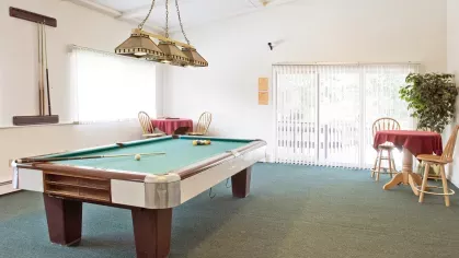 Billiards room at Royal Crest Estates Marlboro with pool table, wall-mounted cue rack, and sliding glass doors leading to outdoor space.