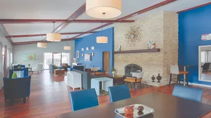 Community clubhouse at Royal Crest Estates Marlboro with dining tables, blue accent wall, large stone fireplace, and lounge seating