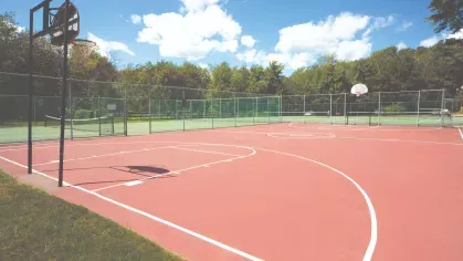 Community basketball court with red surface and fenced tennis courts in the background at Royal Crest Estates Marlboro.
