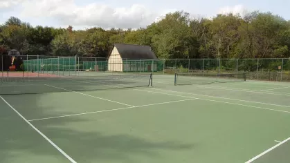 Multiple fenced tennis courts with green playing surface and clubhouse building nearby at Royal Crest Estates Marlboro.
