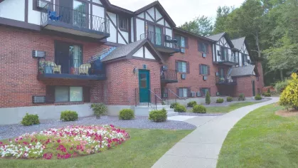 Tudor-inspired apartment exterior with balconies, red brick, and flower garden near walkway at Royal Crest Estates Marlboro.