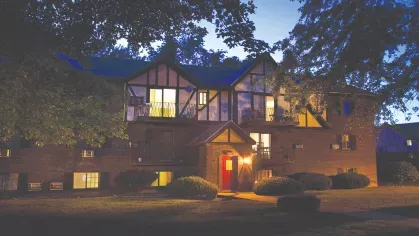 Tudor-style apartment building illuminated at dusk with balconies and lit red entry door at Royal Crest Estates Marlboro.