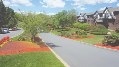 Entrance road lined with landscaped greenery, trees, and Tudor-style apartment buildings at Royal Crest Estates Marlboro.