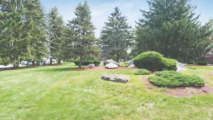 Open green lawn with tall evergreen trees and large decorative rocks at Royal Crest Estates Marlboro