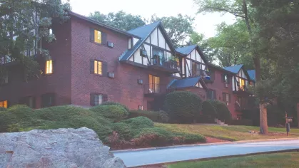 Brick Tudor-style apartment building at dusk with lit windows and mature trees at Royal Crest Estates Marlboro