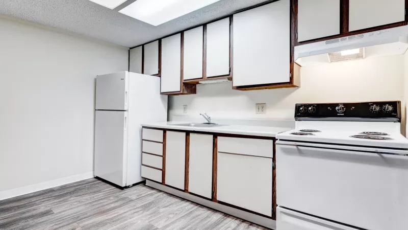 Galley-style kitchen featuring wood-trim cabinetry, white refrigerator and stove, laminate countertops, and plank-style flooring.