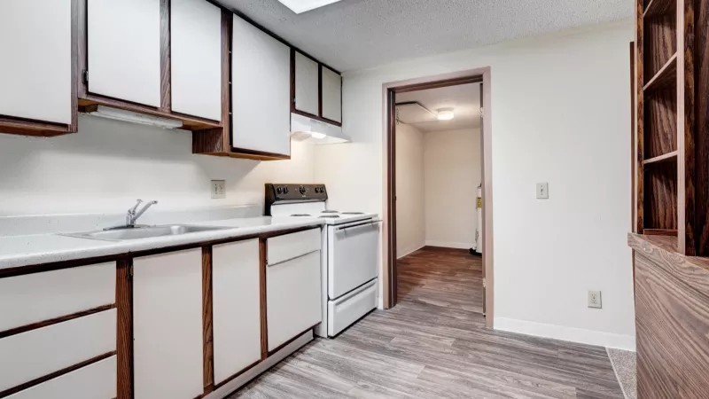 Kitchen with electric range, refrigerator, and ample cabinet storage leading to a utility room with wood flooring.