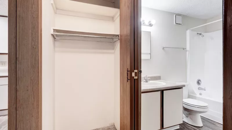 Hallway closet with built-in shelving next to bathroom with single vanity, mirror, and tub-shower combination.