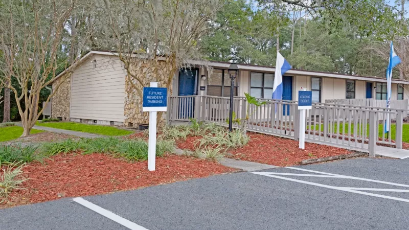 One-story leasing office with stone accents, landscaped grounds, and designated future resident parking spaces.