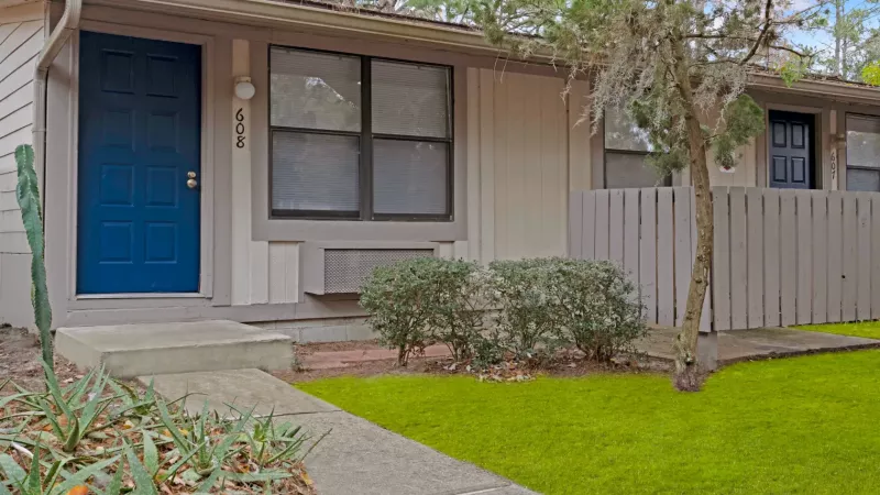 Single-story apartment home with blue front door, fenced patio area, and landscaped walkway.