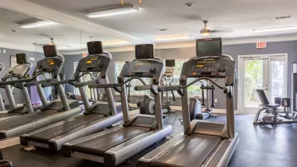 Large gym with multiple workout machines and ceiling fans. 