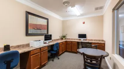 Business center with a large desk that has multiple seats and computers for residents to enjoy.