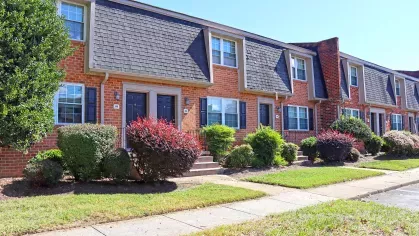 Townhome building at Maple Bay Apartment Townhomes with red brick exteriors, black shutters, and mature landscaping along a clean concrete walkway.