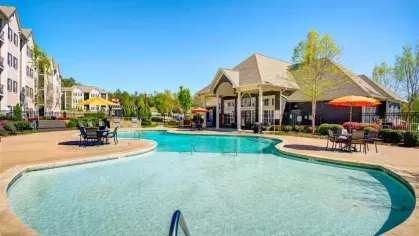 A poolside view, showing a seating area and the swimming pool with water fountains. An outdoor grilling station is visible in the background.