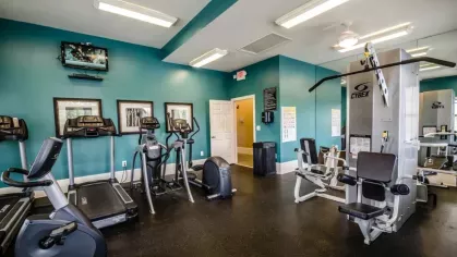 The cardio area of the fitness center, equipped with treadmills, ellipticals, and a stationary bike. A weight machine is visible in the mirrored wall.