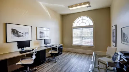 The resident business center, with two computer workstations along a built-in desk. A separate table holds a community printer for resident use.