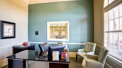 The community leasing office, showing a leasing agent's desk and comfortable guest chairs. A large window and teal accent wall brighten the space.