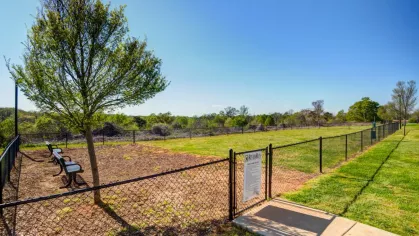 The community's pet-friendly, fenced-in dog park. The large, grassy area includes a bench and a separate wood-chip section for pets to play.