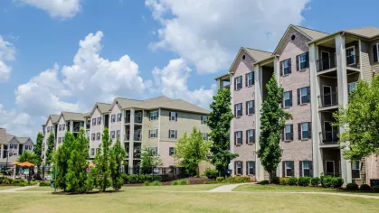Four-story apartment buildings with private balconies surrounded by green lawns and trees.