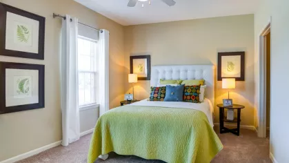 Sunny bedroom with white curtains, green bedspread, and matching bedside lamps.