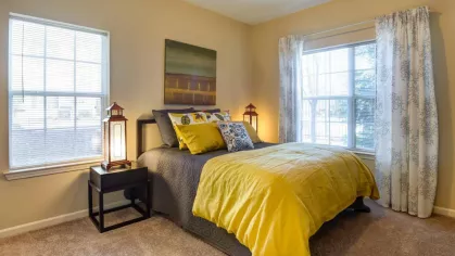 Second bedroom with yellow and gray bedding, large windows, and modern décor.
