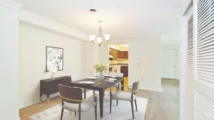 Elegant dining room with dark wood table and light gray chairs, adjacent to an updated kitchen with stainless appliances.