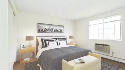 Bright bedroom with a large window, gray bedding, and matching nightstands with lamps on each side of the bed.