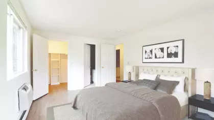 Comfortable bedroom with tufted beige headboard, coordinated bedding, and open doors leading to a walk-in closet and bathroom.