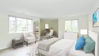 Airy primary bedroom with white furniture, cozy reading chair, and a home office corner near wide windows.