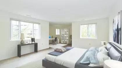 Elegant master bedroom combining a low-profile leather bed, workstation area, and soft natural light from multiple windows.