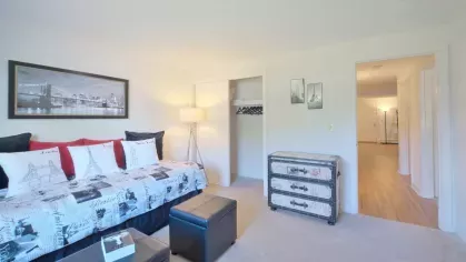 Cozy guest room with patterned bedding, framed city artwork, and carpeted flooring connecting to the hallway.