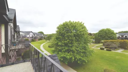 Scenic view from a private balcony overlooking manicured lawns, walking paths, and Tudor-style apartment buildings.