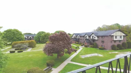 Community courtyard featuring landscaped green space, mature trees, and red-brick apartment homes in Tudor design.