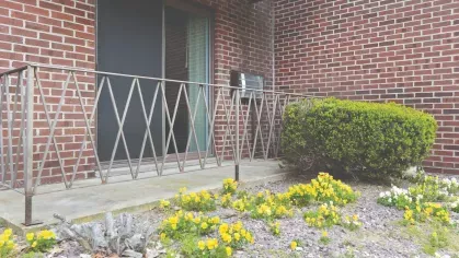 Ground-level patio with brick exterior, metal railing, and blooming yellow flowers along the walkway.