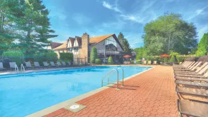 Sparkling outdoor swimming pool surrounded by lounge chairs and shaded seating near the clubhouse.