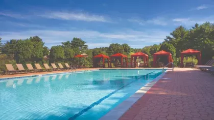 Large swimming pool bordered by lounge chairs and cabanas, set against a backdrop of greenery.