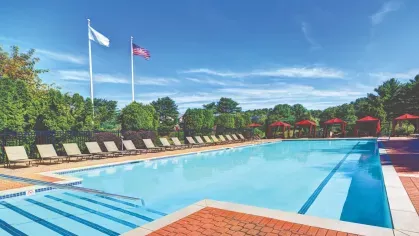 Poolside view with American and community flags flying above lounge chairs and cabanas.