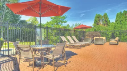 Patio area with outdoor furniture, red umbrellas, and lounge chairs surrounded by black iron fencing.