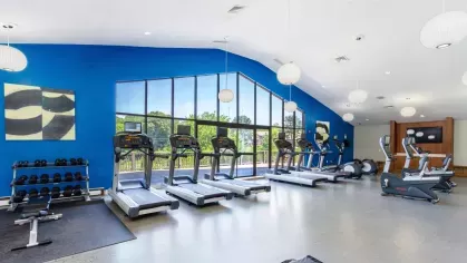 Fitness center with treadmills, stationary bikes, and floor-to-ceiling windows overlooking the property grounds.