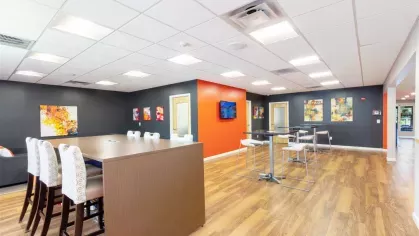 Study and coworking space with tall tables, barstools, and vibrant accent walls in orange and gray tones.