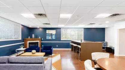 Social lounge with sectional seating, patterned rug, and workspace-style bar near windows.